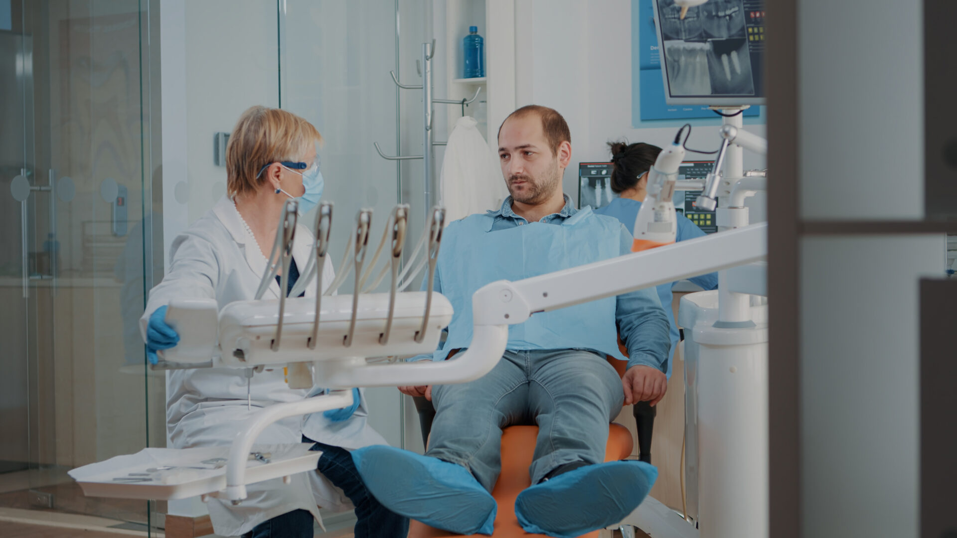A male patient sitting in a dental chair speakingwith a female dentist in a clinical office.